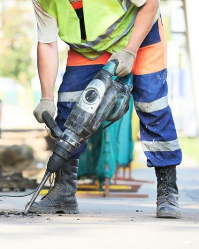 Builder worker with pneumatic hammer drill equipment breaking asphalt at road construction site